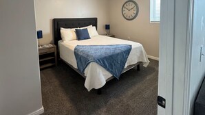 A bedroom with a bed, a nightstand, a wall clock, and a ceiling light.