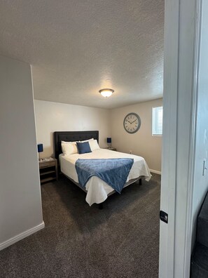 A bedroom with a bed, a nightstand, a wall clock, and a ceiling light. - Walk to Downtown | Sleeps 6 | King Bed + Parking (Logan)