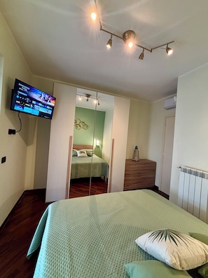 Ein Schlafzimmer mit einem Bett, einem an der Wand montierten Fernseher, einem Kleiderschrank und einem Spiegel.