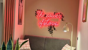 A cozy living area with a sofa, a table with a plant, a lamp, and a neon sign on the wall. - Mazzini28, A1 Caserta North, Royal Palace, concerts, Naples, coast, southern Italy (Casapulla)