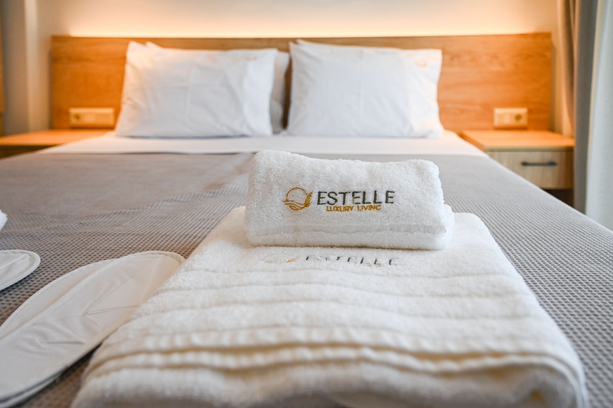 En snyggt bäddad säng med vita sängkläder och en handduk med texten ”ESTELLE LUXURY LIVING”.