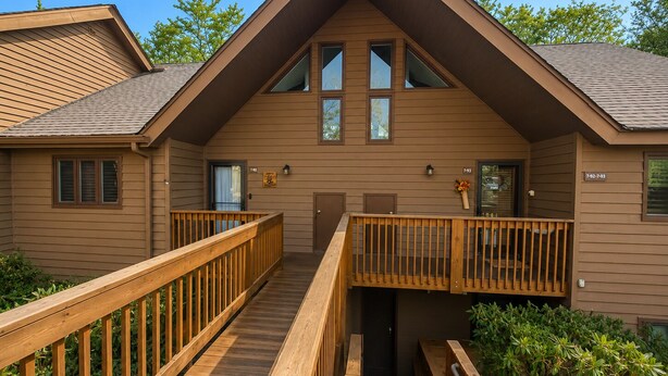 Un chalet à deux étages avec une façade en bois, un balcon à l’étage supérieur et une terrasse en bois menant à l’entrée.