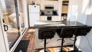 Une cuisine moderne dotée d’un îlot central, de tabourets de bar, d’un réfrigérateur, d’un four à micro-ondes, d’un four et d’une porte-fenêtre coulissante donnant sur un espace extérieur.