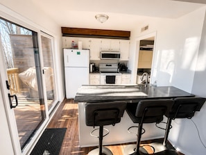 Cocina moderna con una isla central, taburetes de bar, refrigerador, microondas, horno y una puerta corrediza de vidrio que da a un área exterior.