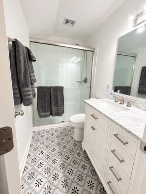 Een badkamer met douche, toilet en wastafel met spiegel.