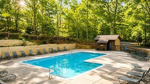 Une piscine rectangulaire avec une terrasse en bois, entourée de chaises longues et d’une petite structure en bois.