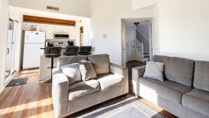 Un salon moderne avec deux canapés, un coin repas avec une cuisine en arrière-plan et un escalier menant à un autre niveau.