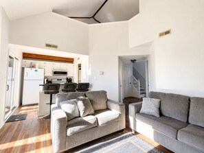 Een moderne woonkamer met twee banken, een eethoek en een keuken op de achtergrond, en een trap naar een ander niveau.