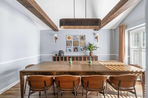 A dining area with a wooden table, chairs, a hanging light fixture, wall art, and a potted plant. - Spacious Retreat w/ Hot Tub & Games | Sleeps 16 (Columbus)