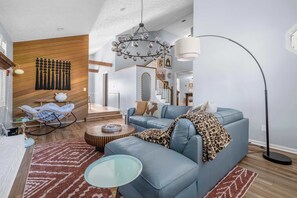 A modern living room with a blue sofa, a glass coffee table, a hanging chandelier, and a floor lamp.