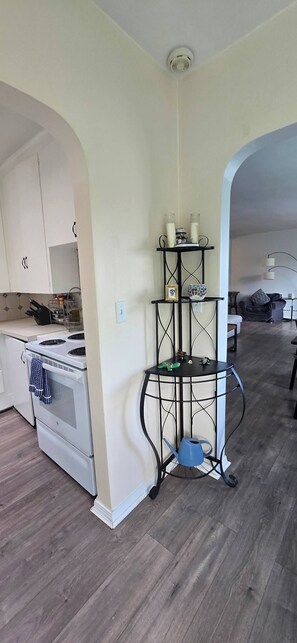 Una cocina con armarios blancos, una estufa y una repisa metálica negra con objetos decorativos.