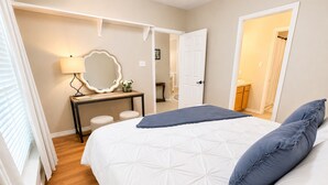 Un dormitorio con cama, mesita de noche, espejo y una puerta que da a otra habitación.