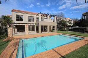 Uma casa moderna de dois andares com piscina, pilares de pedra e pérgola.