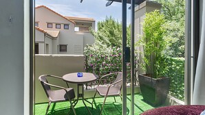 A balcony with a table and chairs, a potted plant, and a view of a building with a tiled roof. - Zalari Loft B, Nature-inspired 2 Bed Loft Paulshof (Johannesburg)