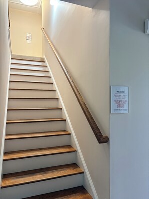 Eine Treppe mit Holzstufen und Geländer, ein Schild an der Wand und eine Leuchte oben.