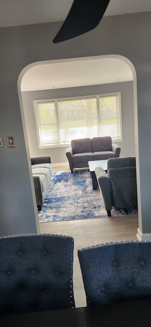 Una sala de estar con un sofá gris, un tapete azul y un ventilador de techo.