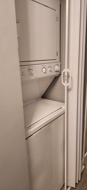 Un appareil combiné lave-linge et sèche-linge blanc, fixé au mur, doté de boutons de commande et d’une poignée de porte.
