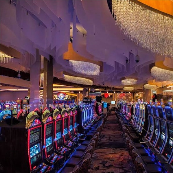 Fila de máquinas tragamonedas en un casino con suelo alfombrado y candelabros.