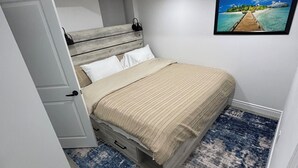 Una camera da letto con un letto, un comodino, una cassettiera, un quadro e un pavimento in legno.