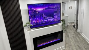 Un soggiorno moderno con una televisione a schermo piatto montata su una parete bianca, un camino sottostante e un pavimento in legno.