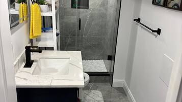 A bathroom with a white sink, a glass shower enclosure, a towel rack with yellow towels, and a small shelf with toiletries.