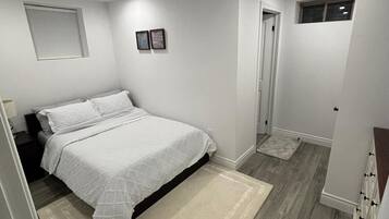 A bedroom with a bed, a nightstand, a door, and a small window.