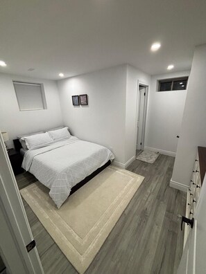 A bedroom with a bed, a nightstand, a door, and a small window. - Luxury Guest Suite (Thorold)