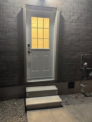 A white door with a window, a metal handrail, and steps leading to the door. - Luxury Guest Suite (Thorold)