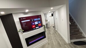 Un soggiorno moderno con una TV a schermo piatto montata a parete, un caminetto sottostante e una scala sulla destra.