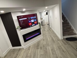 Un salon moderne avec un téléviseur à écran plat fixé au mur, une cheminée en dessous et un escalier sur le côté droit.