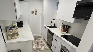 Una cucina compatta con mobili bianchi, un piano di lavoro nero, un lavello in acciaio inossidabile e un forno integrato.