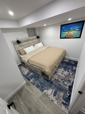 Une chambre à coucher avec un lit, une tête de lit, un tableau et un tapis bleu à motifs.
