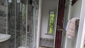 A bathroom with a glass shower enclosure, a sink, and a door leading to a room with a window.