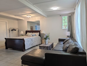 A bedroom with a bed, a sofa, a small table, a mirror, and a window with curtains.