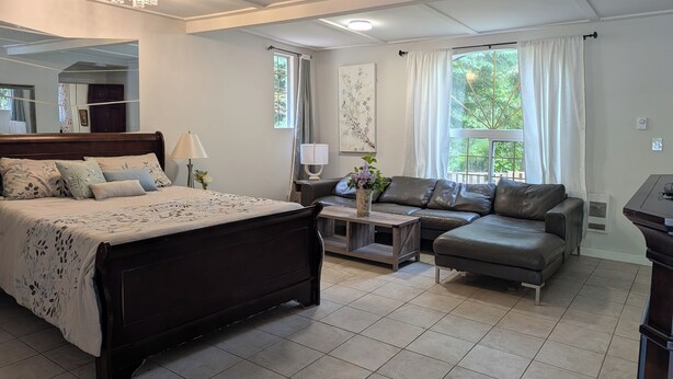 A bedroom with a bed, a sofa, a nightstand, a lamp, and a window with curtains.