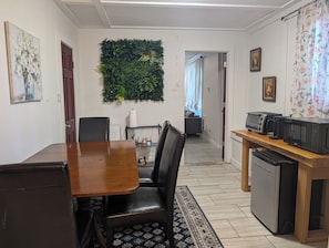 Ein Essbereich mit Holztisch und -stühlen, eine Küche mit Geräten sowie eine grüne Wanddekoration.