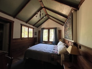A bedroom with a wooden bed, a chandelier, a large window, and a painting on the wall.
