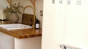 Una cucina con un frigorifero bianco, mensole in legno, un lavello e un vaso con fiori secchi.