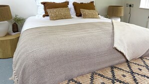 Un letto rifatto con lenzuola a motivi, due abat-jour e un elemento decorativo appeso al muro.