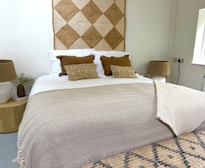 Cama bem arrumada com roupa de cama estampada, duas luminárias de cabeceira e um objeto decorativo na parede.