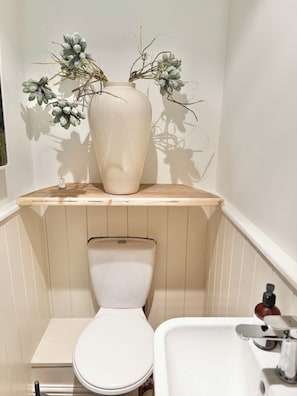 Casa de banho com sanita, lavatório e um vaso com flores secas numa prateleira.
