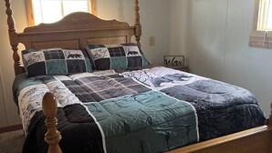A bedroom with a wooden four-poster bed, a quilted bedspread, an air conditioning unit, a window with blinds, and a wall clock.