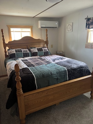 Een slaapkamer met een houten hemelbed, een gewatteerde sprei, een airconditioner, een raam met zonwering en een wandklok.