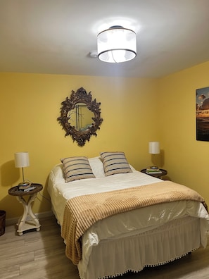 Een kamer met een bed, twee nachtkastjes met lampen, een spiegel en een schilderij aan de muur.