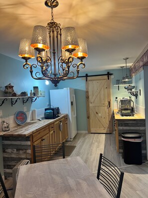 Een keuken met een kroonluchter, houten kasten, een eettafel en een schuifdeur van hout.