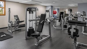 Uma academia com diversos aparelhos de exercício, uma bola vermelha de ginástica e halteres.