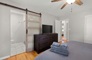 Ein Schlafzimmer mit Bett, Kommode, Fernseher, einer Schiebetür und einem Deckenventilator.