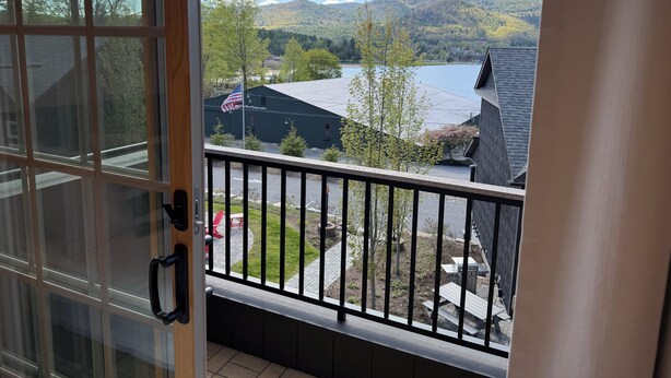 En balkon med udsigt over et sølandskab, træer og en bygning med et amerikansk flag.