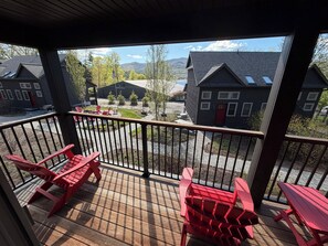 A wooden deck with red Adirondack chairs, a view of buildings, and a paved area with trees. - Deluxe Lodge Lakefront On Lake George #2 (Lake George)