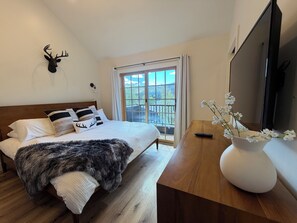 Une chambre à coucher avec un lit, une tête de cerf fixée au mur, une grande fenêtre, un bureau en bois et un téléviseur.